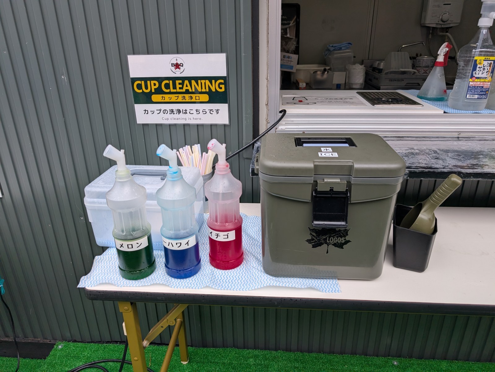 ドリンクブースの端。かき氷のシロップ3種と、氷のクーラーボックスが置かれています
