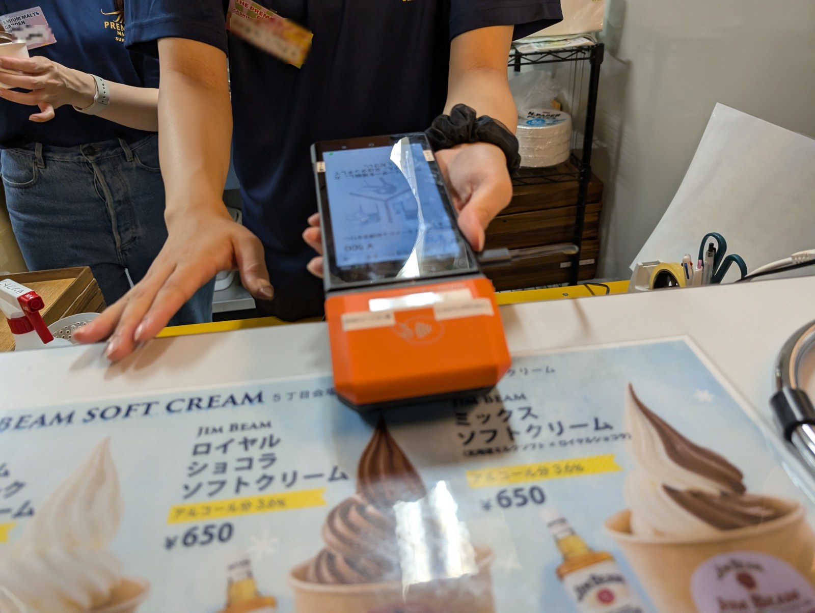 サントリー会場でカードリーダー端末を差し出すスタッフ、手前にジムビームソフトクリームのメニュー