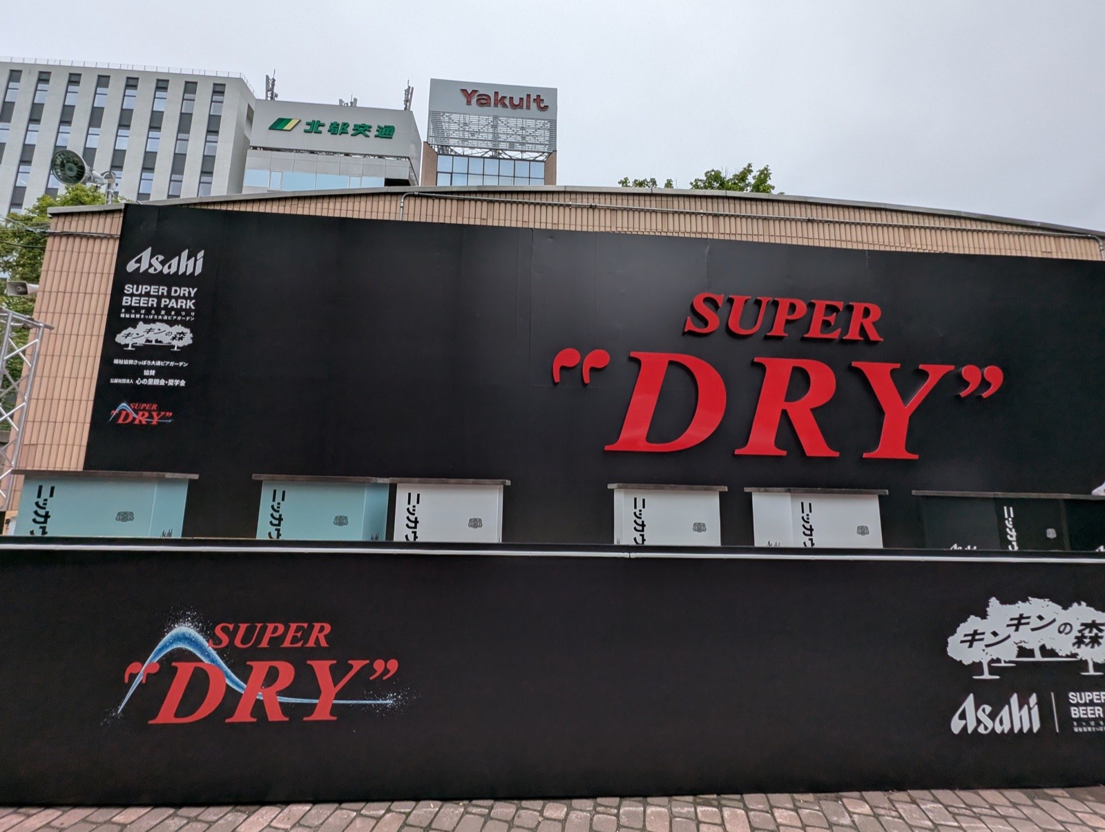 巨大なSUPER DRYのロゴ壁と、手前に並ぶニッカウヰスキー表記のスタンディングカウンター