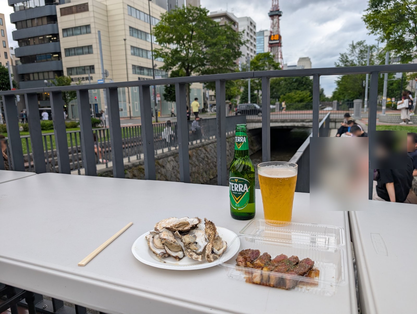牡蠣・肉・生ビールを川床席で。奥にはテレビ塔と創成川が広がります